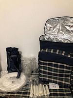 Picnic backpack opened showing insulated interior, plastic plates, glassware, cutlery, and bottle cooler bag.