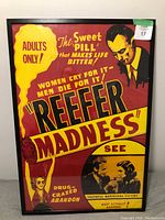 Front view of large framed poster titled 'Reefer Madness' with bold red and yellow colors, black frame, and artwork of a man and woman along with text and warning labels.