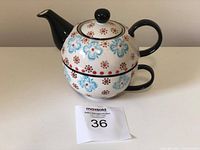 Stacked teapot and cup showing floral pattern and black handles