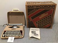 Beige Smith-Corona Majestic 700 portable typewriter displayed open with keys visible, next to original box and instruction manual.