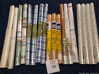 Photo of 18 rolls of self-adhesive drawer liner arranged side by side showing multiple patterns including plaid, wood grain, solid, and decorative prints.