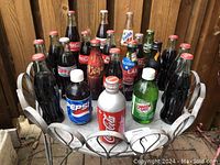 Photo of 20 vintage soda bottles arranged in a metal tray, shows front view of various brands including Coca-Cola, Pepsi, Fanta, and others.