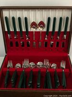 Full open view of flatware set in wooden box showing all utensils with green handles and serving spoons