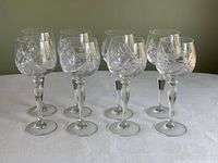 Front view of 8 crystal wine glasses showing pinwheel and floral etched patterns and faceted stems.