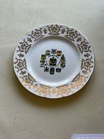 White ceramic plate with gold ornate border and Canada coats of arms crests in center