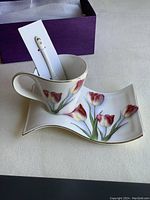 Cup, spoon, and snack tray in purple box with the cup on the tray displaying floral tulip pattern with gold rim and the spoon upright inside the cup.