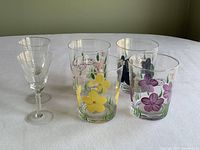 Photo showing 2 clear Aperitif glasses and 4 Garden Country hi-ball glasses with floral designs arranged on a table.
