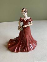 Front view of the porcelain figurine showing the lady in a red dress holding a bouquet.