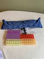 Microwaveable blue floral neck warmer accompanied by multiple pill organizers and droppers in sealed plastic bags.