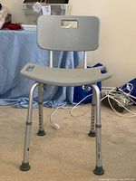Adjustable shower chair with gray plastic seat and backrest, aluminum legs with rubber tips and height adjustment holes.