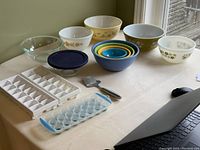 Overview of all items arranged on table including Pyrex bowls, nested plastic bowls, cheese slicer, and ice cube trays
