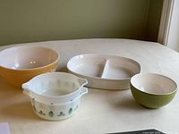 View of all four items: large yellow Pyrex bowl, white divided Corning Ware dish with green leaf pattern, small green bowl, and small white interior bowl