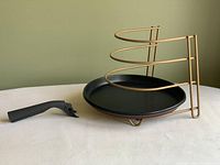 Non-stick black round pan with detached black handle and gold-tone spiral rack beside it on the table.