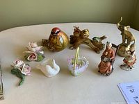 Nine assorted decorative pieces including a brass elephant bell, bird figurines, flower decor, elderly figurines, and a heart-shaped 'Love' bird decoration.