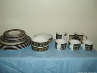 Full set laid out on light blue tablecloth, showing all items including plates, bowls, and cups with detailed motifs.