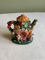 Front view of the ceramic teapot piggy bank with three bunny figurines and floral decorations.