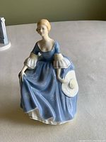 Front view of the Royal Doulton Hilary porcelain figurine seated, holding a hat, wearing a blue dress with star patterns.