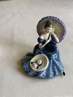 Front view of seated woman figurine holding parasol and hat on lap