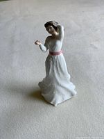 Front view of Royal Doulton porcelain figurine woman holding a flower in hand wearing a white dress with pink sash.