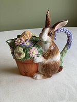 View of ceramic bunny holding flower pot front and side showing detailed flowers and crack on pot