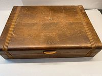 Closed wooden case with horizontal grooved decorative lines and a small handle for opening