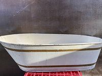 White oval metal washbasin with gold stripes on exterior, showing wear and chipping paint.