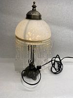 Front view of the glass shaded lamp showing white glass shade, metal base, and beaded fringe trim.