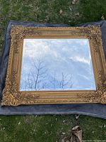 Full view of the rectangular mirror showing its ornate, gold-colored detailed frame and reflective glass surface.
