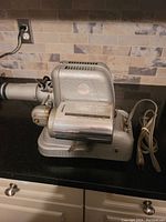 Side view of heavy vintage projector showing metallic body, ventilation slots, long lens tube, and attached power cord