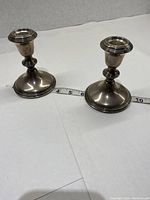 Pair of Empire style sterling silver weighted candle holders placed on a white surface next to a measuring tape showing size approx 4 inches tall.