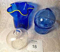 Three art glass vases: wavy blue kerchief vase with yellow rim, stacked blue spheres vase, and clear ball vase.