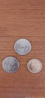 Three American coins on a wooden surface: two Kennedy half dollars and one Sacagawea dollar coin, reverse sides visible showing eagle and other designs