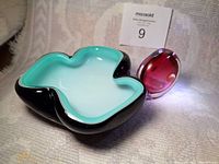 Photo showing organic shaped art glass bowl with turquoise inside and black outer layer alongside the pink rounded bud vase with orange dot detail