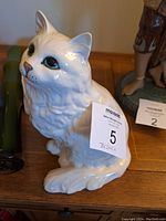 White Beswick Persian cat figurine, front and slightly left side view showing cat looking up with green eyes and pink nose, seated on wooden surface with Beswick label number 5 attached.