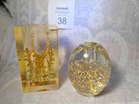 Two collectible items shown together: Lucite cube with golden Korean Silla crown replica and clear Murano glass paperweight with gold aventurine decoration.