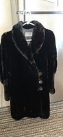 Front view of the black fur coat hanging on a hanger, showing button closure and fur texture.