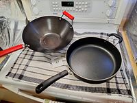 Wide shot of the wok and frypan side by side on a cloth-covered stove.