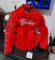 Red Rocket motorcycle jacket laid on a surface showing full front view with embroidered sleeve and multiple zipper pockets.