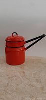 Front side view of the red enamelware double boiler pot showing both stacked pots and the lid with handle on top, along with long black handles.