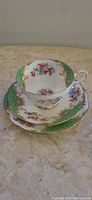 Teacup, saucer, and plate set with green floral pattern and gold accents shown stacked together.