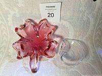 Photo showing the pink clover-shaped glass bowl and clear glass ashtray side by side on a white textured cloth.