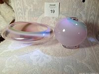 Two pink-toned handblown glass pieces: one ball-shaped and one shallow bowl-shaped on cream fabric background