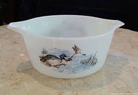 Side view of white milk glass Pyrex casserole with Waterfowl pattern showing ducks in a pond with grass and reeds.