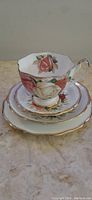 Porcelain teacup stacked on saucer and two plates, showing floral rose design and gold trim