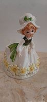 Full view of ceramic girl planter showing her white dress, green bodice, bonnet, and floral base