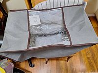 Open large soft storage bag showing clear plastic window, zipper, grey fabric with brown edge trim.