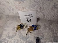 Two vintage goldtone brooch pins with blue satin shoe buttons and filigree leaves, displayed with auction number card.