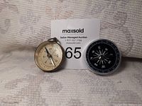 Photo of the two compasses, the vintage brass fob compass and the modern black compass side by side.