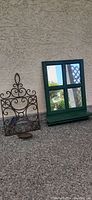 Photo of both items - wrought iron candle sconce and green windowpane-style mirror shelf, placed against a textured wall.