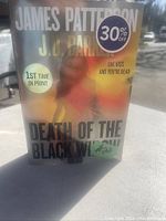 Front cover of the 2022 book 'Death of the Black Widow' by James Patterson and J.D. Barker with discount and price stickers visible.